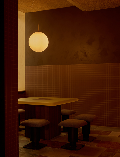 Warm interior with tiled walls, pendant light, and a table surrounded by stools